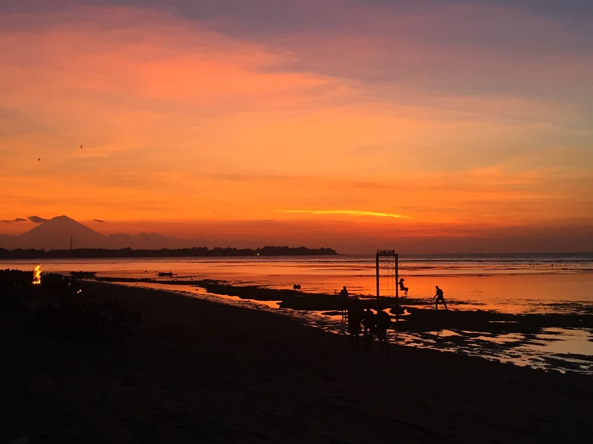 People silhouetted along a shoreline at sunset