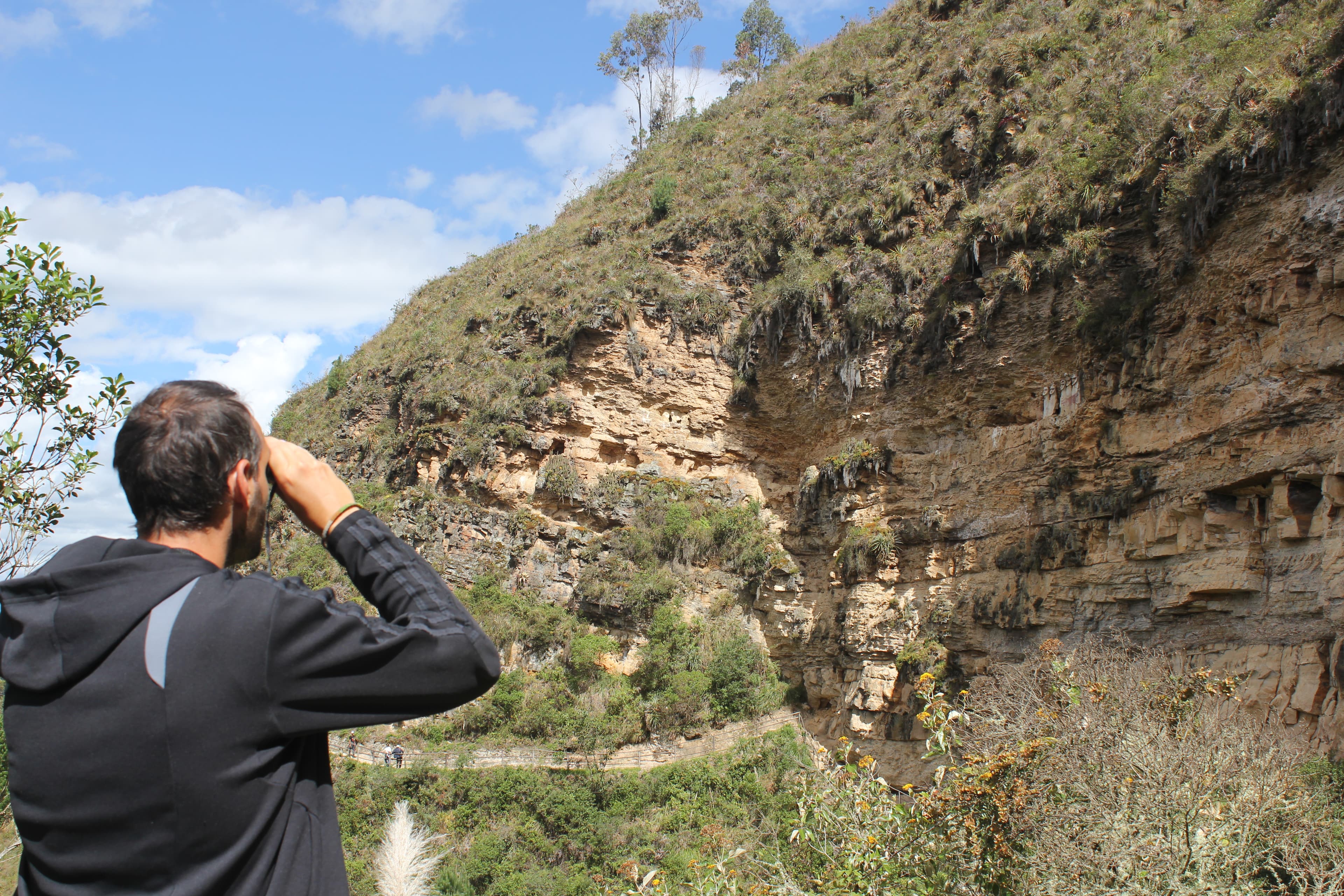 A traveller looking through binoculars toward the Karajía sarcophagi cliff