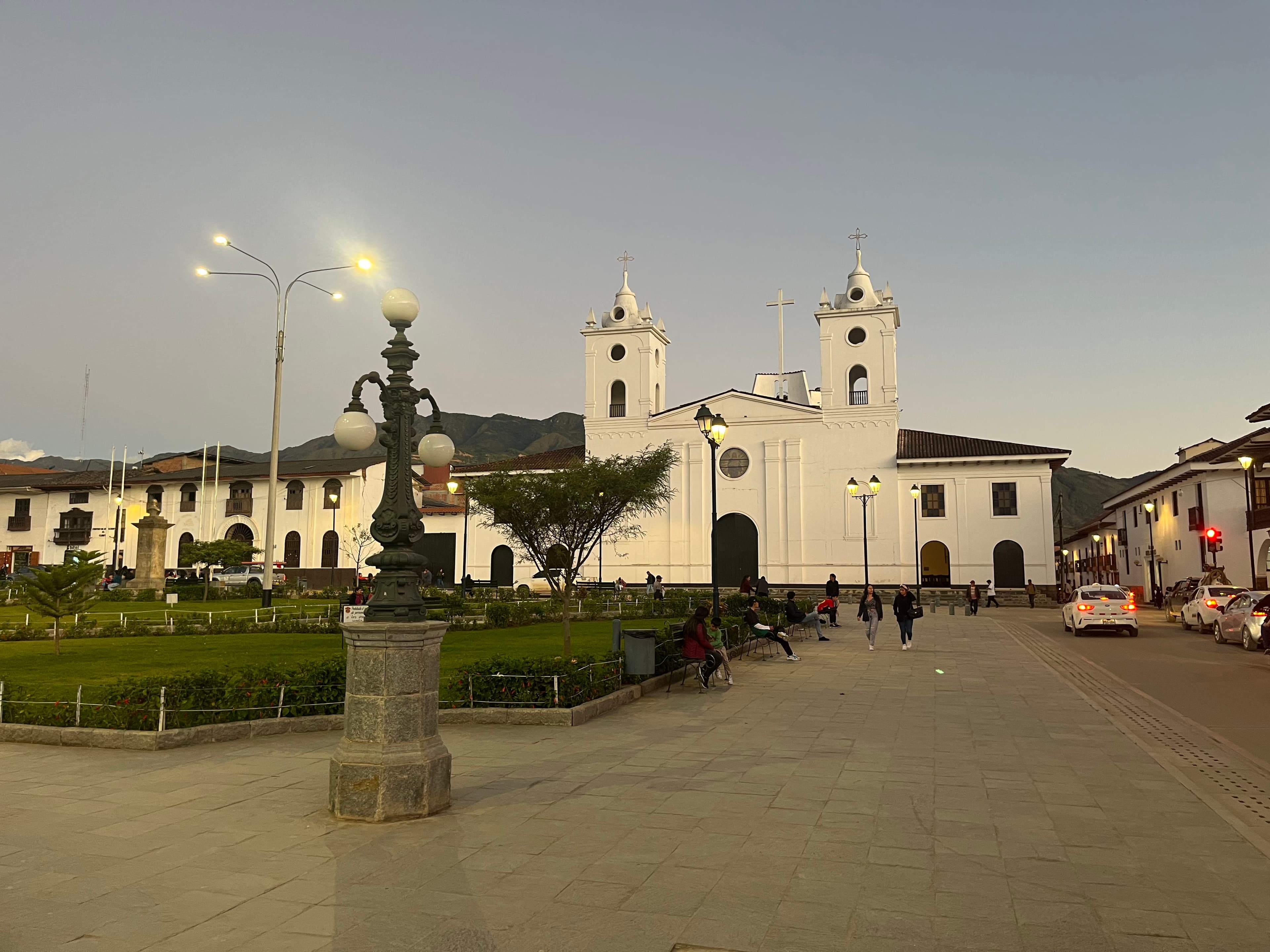 People in a town square beside a white church at dusk