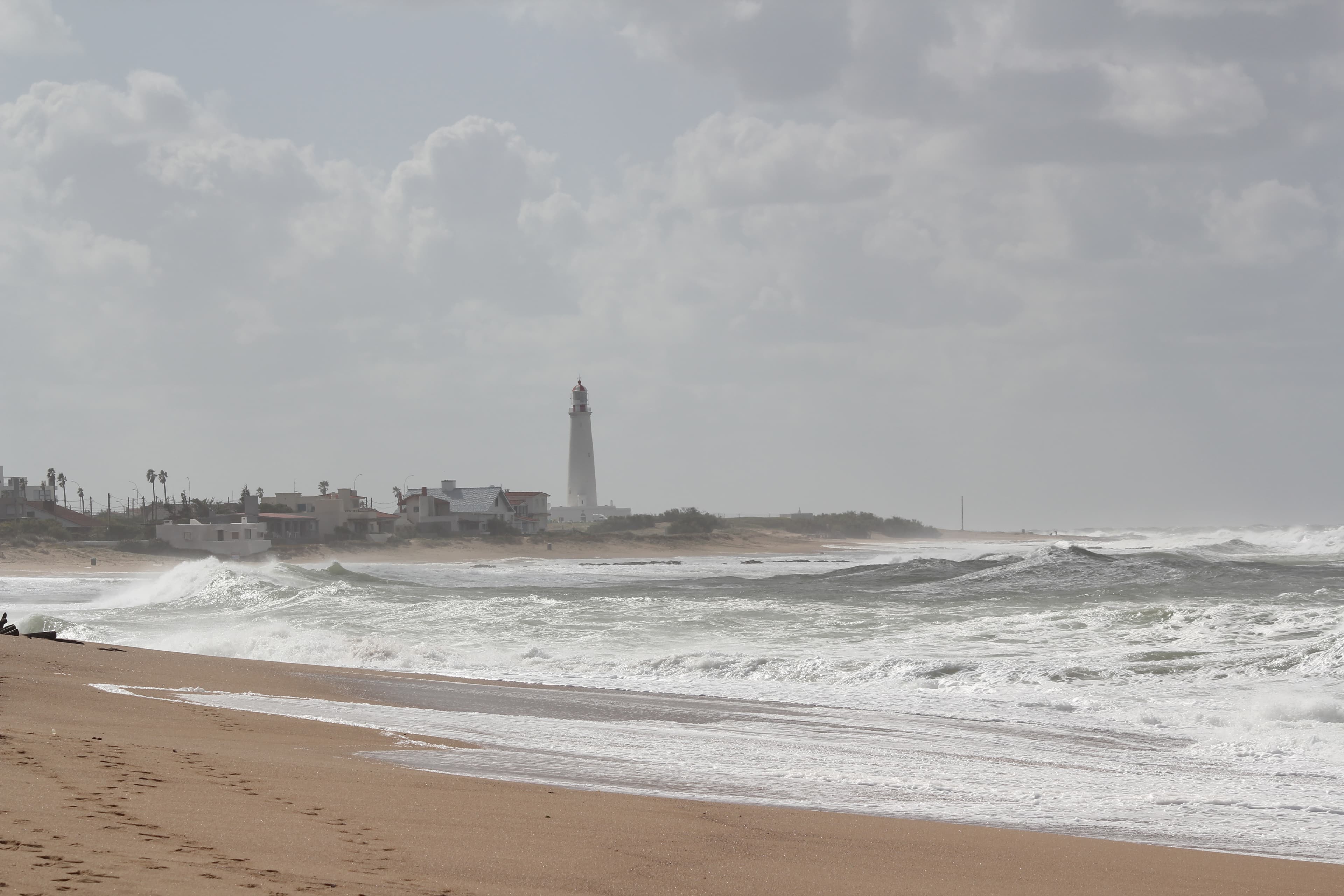Windy Atlantic shoreline with a distant lighthouse under a pale sky